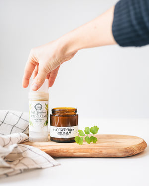 Full Spectrum CBD Balm 2.5 oz twist up tube and oz amber glass jar with hand reaching in to grab