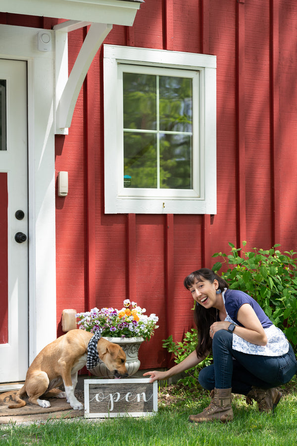 The Little Flower Soap CO Open sign with puppy and founder Holly Rutt outside red barn retail shop in Chelsea Michigan