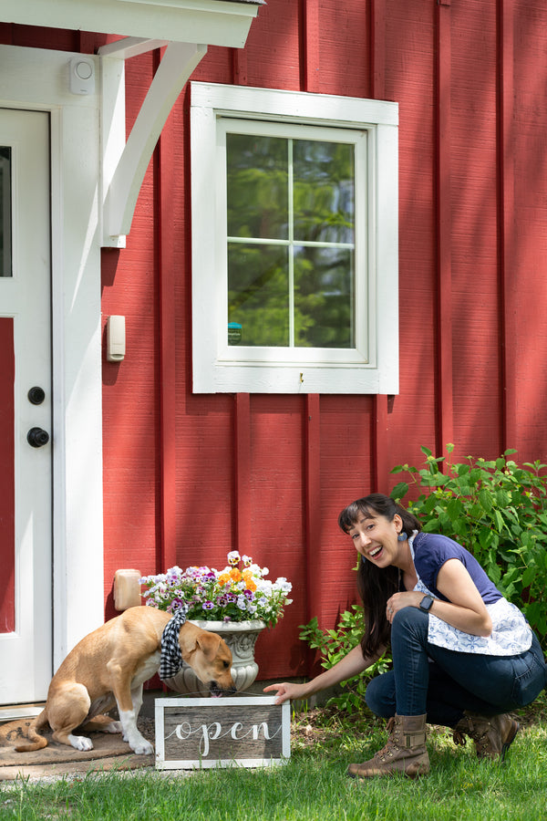 The Little Flower Soap CO Open sign with puppy and founder Holly Rutt outside red barn retail shop in Chelsea Michigan red barn studio handmade soap and gifts shop