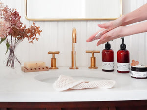 luxury liquid hand soap and lotion essential oil in decorative amber pump bottles at brass vintage farmhouse style bathroom sink with natural decor and hands washing in running water