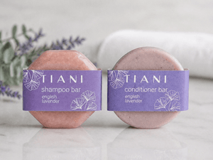 Two Tiani shampoo and conditioner bars on a white surface with lavender leaves in the background.
