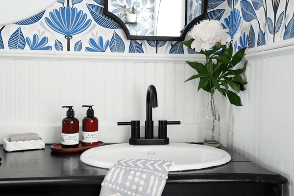 marble soap dish scalloped for large 6oz bar soap in a beautiful farmhouse bathroom with wainscoting and blue floral wallpaper black faucet and old black dresser sink.  essential oil liquid soap and lotion and an ikat blue and white turkish cotton hand towel