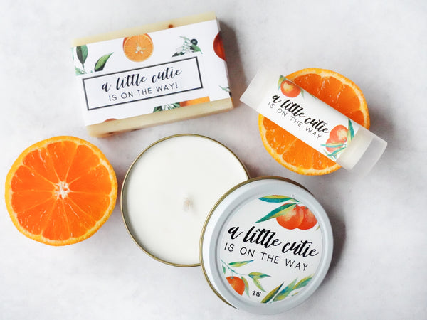 Baby shower favors for a little cutie is on the way theme with soap chapstick and candle pictured with oranges and featuring watercolor clementine tangerine graphics.